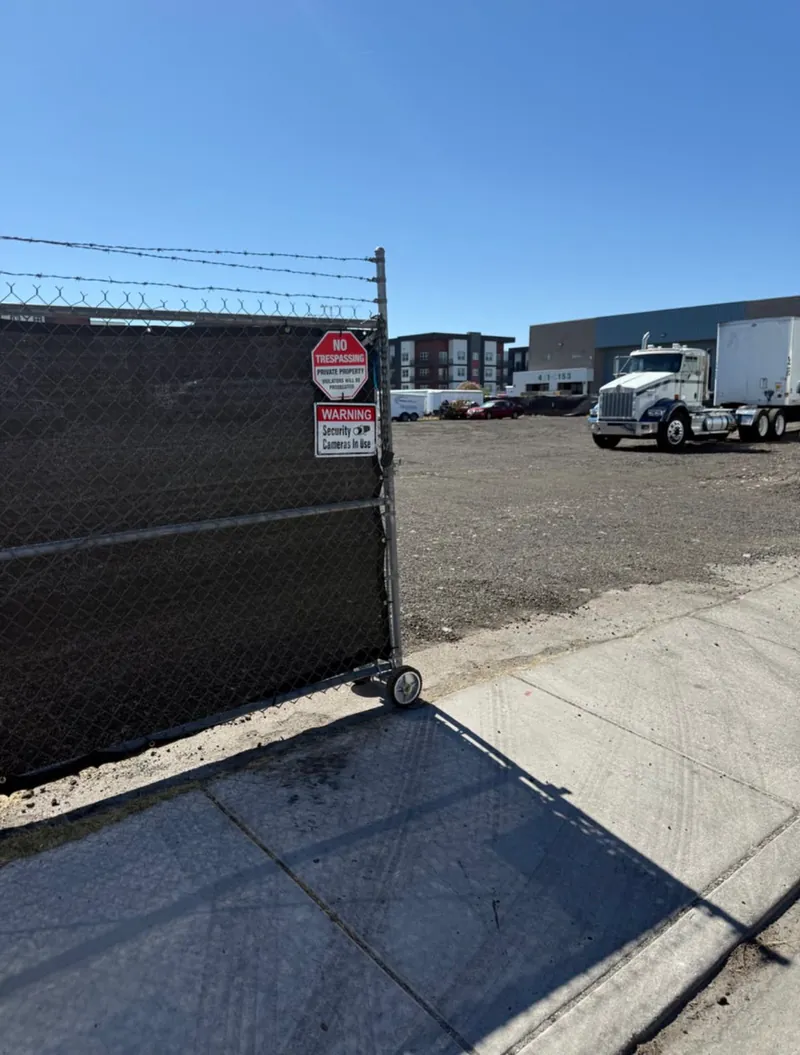 Gated entrance with privacy-screened, barbed-wire perimeter fencing and security camera signage at the Strip Yard in Las Vegas